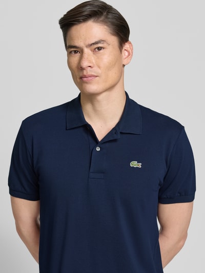 Männermodel trägt Regular Fit Poloshirt aus Baumwoll-Mix von Lacoste in Unifarben Dunkelblau mit Logo-Detail, Nahaufnahme Oberkörper.