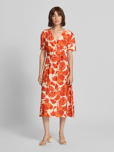 Vrouwenmodel draagt midi-jurk uit viscosemix met strikceintuur Model 'Si44ciliana' van ZABAIONE, oranje-wit patroon, getailleerd model, V-hals in wikkellook, ruglengte maat S: 109 cm, borstwijdte maat S: 49 cm, mouwlengte maat S: 27 cm, volledig vooraanzicht.