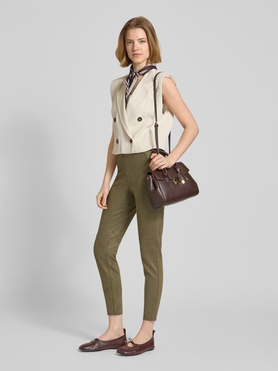 Modelka nosi Slim Fit Hose in verkürzter Passform od Christian Berg Woman, krój slim fit, welurowa faktura, oliwkowy kolor, szerokość w rozmiarze 36: 37 cm, długość nogawki od wewnątrz w rozmiarze 36: 73 cm, widok całej sylwetki z przodu.