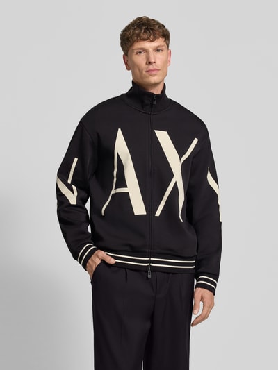 Männermodel trägt Sweatjacke aus Baumwoll-Mix von Armani Exchange, schwarz mit cremefarbenem Label-Print, lockere Passform, Zwei-Wege-Zipper, gerippte Abschlüsse, Ganzkörperansicht von vorne.