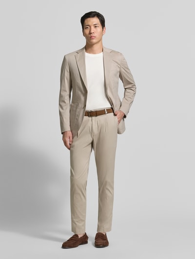 Männermodel trägt Regular Fit Stoffhose mit Logo-Detail Modell 'Lester' von JOOP! Collection aus elastischem Baumwoll-Mix, Bundfalten und Gesäßtaschen, Beige, glatte Textur, Ganzkörperansicht von vorne.