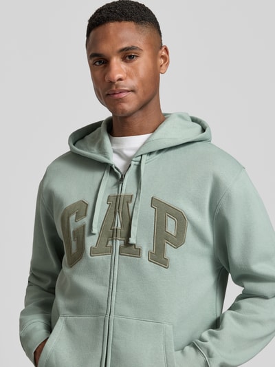 Männermodel trägt Sweatjacke mit Logo und Känguru-Tasche von GAP in Mintgrün, Baumwoll-Mix, Nahaufnahme Oberkörper.