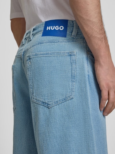 Männermodel trägt Loose Fit Jeansshorts aus reiner Baumwolle Modell 'MASON' von Hugo Blue in Denim-Optik mit Label-Patch, Detailaufnahme Rückansicht.