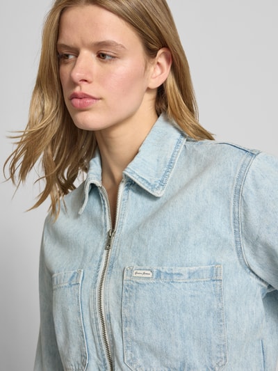Frauenmodel trägt Cropped Jeansjacke mit Reißverschluss von Guess Jeans in Used-Look aus Baumwoll-Lyocell-Mix, Nahaufnahme Oberkörper.