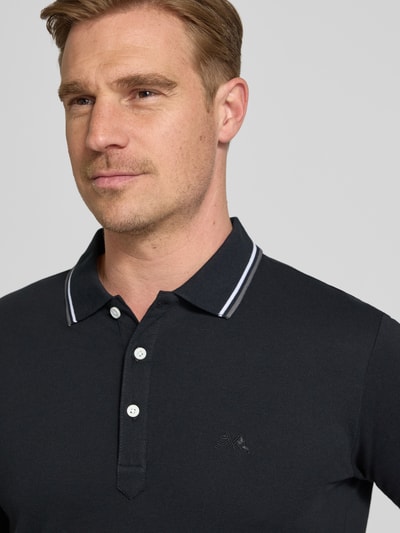 Mężczyznamodel nosi koszulkę polo Relaxed Fit Poloshirt mit Kontraststreifen od Lindbergh z bawełny, paski w kontrastowym kolorze, listwa guzikowa, wyhaftowane logo, długość tyłu w rozmiarze M: 67 cm, zbliżenie na górną część ciała.