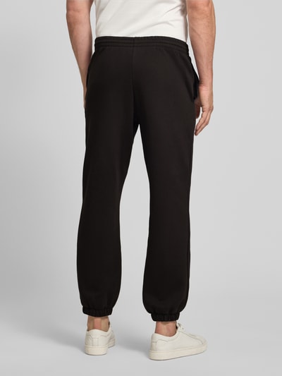 Männermodel trägt Regular Fit Sweatpants aus bawełny-mix von Lacoste, efekt: jednolity kolor, krój regular fit, wyhaftowane logo, tunel wewnętrzny, ściągacz, elastyczne zakończenie nogawek, wpuszczane kieszenie boczne, dzianina dresowa, szczotkowany polar, mieszanka bawełny, ganzkörperansicht rückansicht.