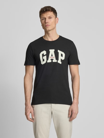 Männermodel trägt T-Shirt mit Logo und Rundhalsausschnitt von GAP in Schwarz, Reine Baumwolle, Regular-Fit, Rückenlänge 69 cm, Ganzkörperansicht von vorne.
