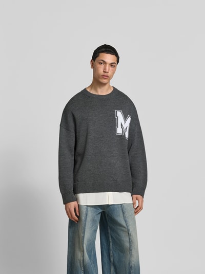 Männermodel trägt Oversized Pullover aus Woll-Mix von MM6 Maison Margiela in Dunkelgrau mit Strick-Optik, Logo-Stitching, Rundhalsausschnitt, Rückenlänge bei Größe M: 80 cm, Ganzkörperansicht von vorne.