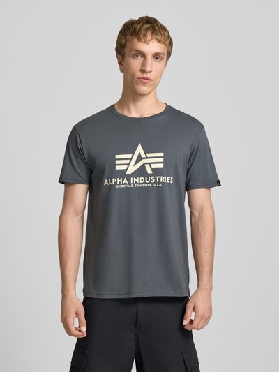 Männermodel trägt T-Shirt mit Logo und Rundhalsausschnitt von Alpha Industries, reine Baumwolle, Regular Fit, grauer Farbton, Ganzkörperansicht von vorne