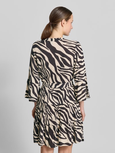 Vrouwenmodel draagt Tailliertes Tunikakleid aus reiner Viskose Modell 'MELBA' van Vero Moda met alloverprint, taillering, minilengte, V-hals, riemlussen, bindriem, trompetmouwen, volantzoom, pure viscose, zwart-beige, geheel lichaam achteraanzicht