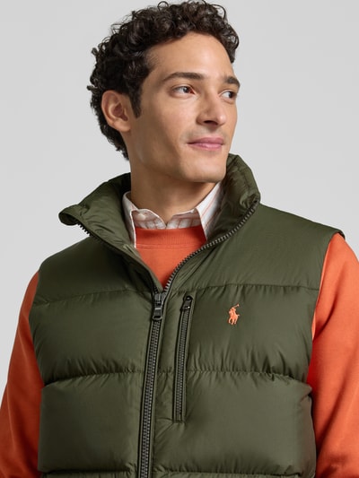 Männermodel trägt olivgrüne Regular Fit Weste mit Logo-Stitching von Polo Ralph Lauren über orangefarbenem Pullover, Nahaufnahme Oberkörper. Herren Weste von Polo Ralph Lauren