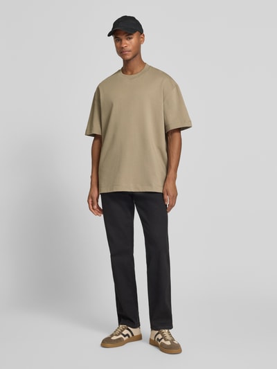 Męski model nosi T-Shirt mit Rundhalsausschnitt Modell 'Carl' od Les Deux z czystej bawełny, prosty krój, detal z logo, beżowy, widok całej sylwetki z przodu.