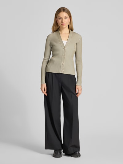 Frauenmodel trägt Strickjacke mit V-Ausschnitt und Knopfleiste von Emporio Armani in Beige, Material-Mix mit Viskose-Anteil, Slim Fit, kombiniert mit schwarzer weiter Hose, feine Rippenstruktur, Ganzkörperansicht von vorne.