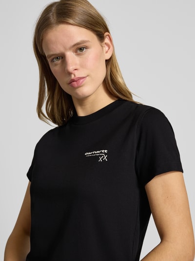 Frauenmodel trägt T-Shirt mit Label-Detail von Carhartt Work In Progress, reine Baumwolle, gerader Schnitt, Rundhalsausschnitt, Nahaufnahme Oberkörper.