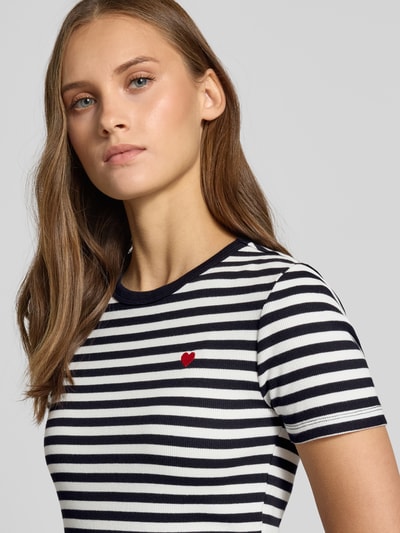 Kobiece model prezentuje damski t-shirt Slim Fit T-Shirt aus Baumwoll-Mix Modell 'VAL' od ONLY w biało-granatowe paski z czerwonym haftem serca, nahaufnahme górnej części ciała.