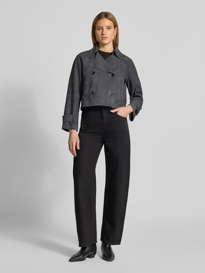 Modelka nosi Regular Fit Trenchcoat aus echtem Ziegenleder od Marc O'Polo w optyce zamszowej, kolor ciemnoszary, długi rękaw, dwurzędowa listwa guzikowa, kieszenie boczne, kołnierz z klapami, wykonany z prawdziwej skóry koziej, krój regular fit, widok całej sylwetki z przodu.