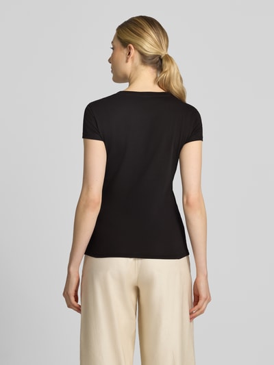 Frauenmodel trägt schwarzes Slim Fit T-Shirt aus Baumwolle von Armani Exchange, glatte Textur, Rückenansicht, Damen T-Shirt, Kontext: Reine Baumwolle, Slim Fit, Rundhalsausschnitt, Label-Detail mit Strasssteinbesatz, Rückenlänge bei Größe S: 59 cm. Ganzkörperansicht Rückansicht.