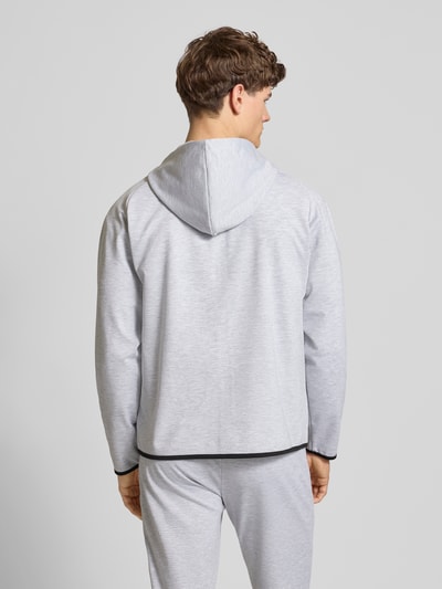 Mannelijk model draagt Regular Fit Sweatjacke mit Kapuze Modell 'Base' van Jack & Jones in lichtgrijs met zijzakken, rugaanzicht, context heren sweatjack, elastische materiaalmix met katoen, rits, capuchon, lengte maat M 66 cm, mouwlengte 70 cm.