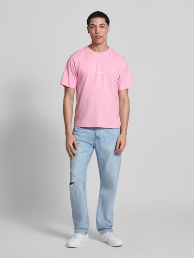 Męski model nosi T-Shirt mit Logo und Rundhalsausschnitt od Jack & Jones, bawełna ekologiczna, krój regular fit, okrągły dekolt, logo, długość tyłu w rozmiarze M: 68 cm, jasnoróżowy, prosty fason, gładka faktura, całkowity widok z przodu.