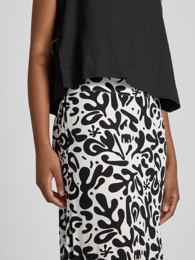 Frauenmodel trägt Maxi-Rock aus reiner Viskose Modell 'BARRI' von Pieces, Optik:Allover-Muster, Passform:Schmal, Bundabschluss:Elastisch, Material:Reine Viskose, Schwarz-Weiß-Kontrast mit abstrakten Formen, glatte Textur, Nahaufnahme Unterkörper.