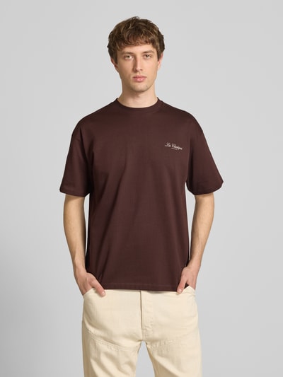Männermodel trägt Loose Fit T-Shirt aus reiner Baumwolle Modell 'LES CLASSIQUES' von Only & Sons, einfarbig braun, Jersey, Schriftzug-Print, Ganzkörperansicht von vorne.