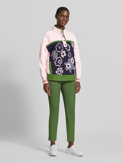 Frauenmodel trägt Relaxed Fit Pullover aus Viskose-Mix mit Troyer-Kragen von Marc Cain, florales Design, grüne Hose, Ganzkörperansicht von vorne. Rückenlänge 62 cm, Ärmellänge 54 cm.
