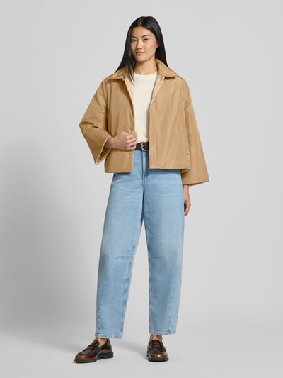 Modelka nosi beżową kurtkę funkcyjną z funkcją dwustronną model 'FALENA' od Weekend Max Mara, jasne dżinsy i brązowe buty, kurtka w kroju regular fit, delikatny połysk, prostokątne kształty, gładka tekstura, przód kurtki rozpięty, widoczne kieszenie, damska kurtka funkcyjna Weekend Max Mara, Ganzkörperansicht von vorne.