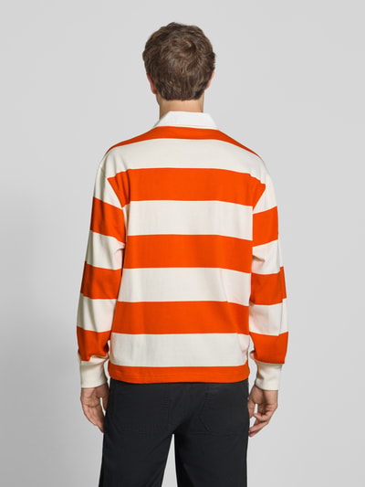 Männermodel trägt Relaxed Fit Poloshirt aus reiner Baumwolle von Champion, breite orange-weiße Streifen, Rückenansicht, Ganzkörperansicht Rückansicht.