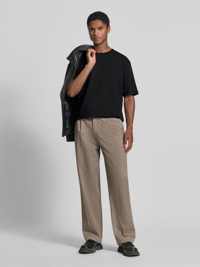 Männermodel trägt Oversized T-Shirt aus reiner Baumwolle von Lindbergh in Schwarz, kombiniert mit beigefarbener Hose, Ganzkörperansicht von vorne.