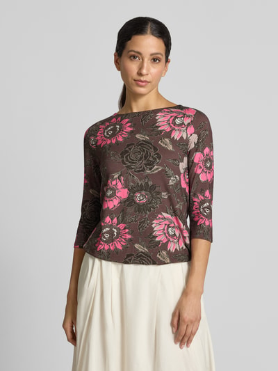 Modelka nosi T-Shirt im Allover-Look mit 3/4-Arm von Christian Berg Woman, mieszanka wiskozy i elastanu, krój slim fit, wzór na całej powierzchni, okrągły dekolt, rękaw o dł. 3/4, Długość tyłu w rozmiarze S: 55 cm, brązowe tło, różowe i beżowe kwiaty, prosta faktura, Ganzkörperansicht von vorne.