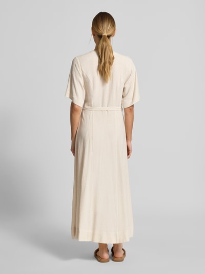 Modelka kobieca nosi Regular Fit Leinenkleid mit V-Ausschnitt Modell 'VIVA' od Selected Femme, beżowy, długi, wiązany pasek, kieszenie, mieszanka wiskozy i lnu, widok całej sylwetki z tyłu.