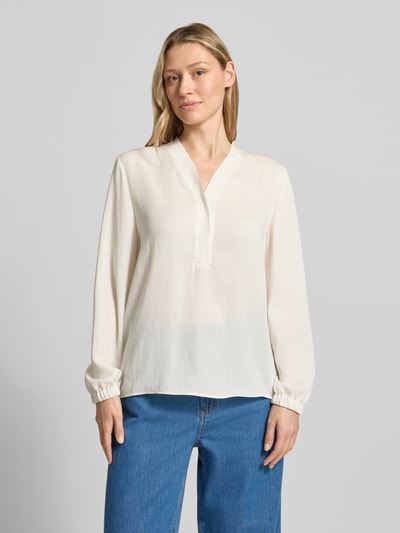 Frauenmodel trägt Bluse mit V-Ausschnitt und Label-Detail von Marc Cain in Creme, lockerer Schnitt, elastische Ärmel, Ganzkörperansicht von vorne.