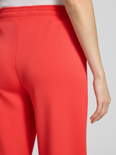 Frauenmodel trägt Wide Fit Sweatpants in verkürzter Passform Modell 'Banu' von Soyaconcept aus Elastischer-Material-Mix mit Modal-Anteil, kräftiges Rot, glatte Struktur, Tunnelzug-Bund, Detailaufnahme Rückansicht.