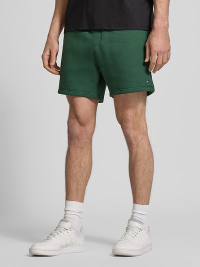 Männermodel trägt Regular Fit Shorts aus Baumwoll-Mix von Tommy Jeans, efekt: jednolity kolor, detal z logo, tunel, elastyczny ściągacz, wpuszczane kieszenie z przodu, kieszeń z tyłu, wykończenie: dzianina dresowa, materiał: mieszanka bawełny, ganzkörperansicht z przodu.