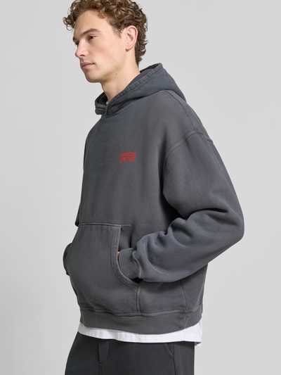 Männermodel trägt hoodie met logo model 'PLIZZY' van American Vintage in donkergrijs, puur katoen, relaxed fit, kangoeroezak, logoprint, ruglengte maat M 66 cm, mouwlengte maat M 60 cm, ganzkörperansicht van voren.