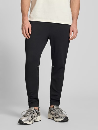 Männermodel trägt Slim Fit Tracksuit mit Logo-Stitching Modell 'Egeo' von SERGIO TACCHINI in Schwarz, elastischer Baumwoll-Mix, Nahaufnahme Unterkörper.