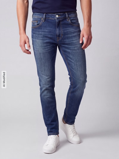 Männermodel trägt Slim Fit Jeans aus Baumwoll-Mix Modell 'Scanton' von Tommy Jeans in Denim-Optik, 5-Pocket, Ganzkörperansicht von vorne, KI-modifiziertes Bild.