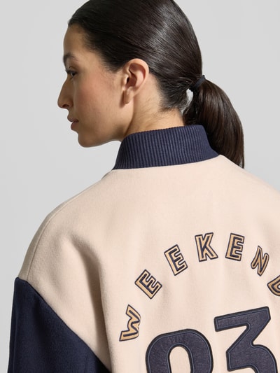 Vrouwenmodel draagt Relaxed fit college-jack uit scheerwolmix model 'ELLISSE' van Weekend Max Mara, look: effen, tweekleurige look, applicatie met labelstitching, drukknopen, collegekraag, lange mouw, geribde mouwboord en rompzoom, zij-steekzakken, detailopname rug.