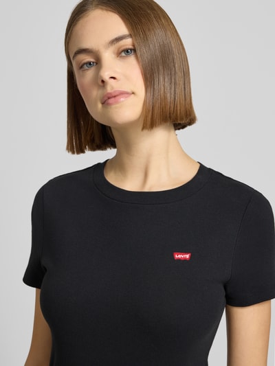 Kobiece model nosi T-shirt z label-patch model 'Cavia' od Levi's®, czarna bawełna, prosty krój, okrągły dekolt, zbliżenie na górę ciała.