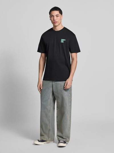 Męski model nosi Relaxed Fit T-Shirt aus reiner Bio-Baumwolle Modell 'FRED' od Only & Sons, czarny, nadruk z przodu, bawełna organiczna, krój relaxed fit, widok całej sylwetki z przodu