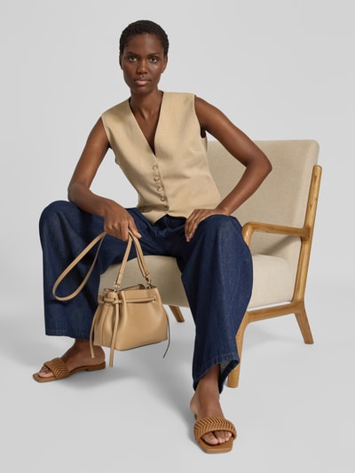 Frauenmodel trägt Handtasche mit Tragehenkel Modell 'Romina' von MANGO in Beige mit Schulterriemen, Hauptfach mit Magnetverschluss, Ganzkörperansicht von vorne.