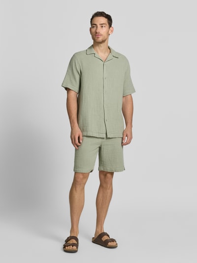 Męski model nosi szorty mit Eingrifftaschen und elastischem Bund von Lindbergh z bawełny, krój loose fit, kolor jasny zielony, całkowity widok z przodu. Szerokość w rozmiarze M: 43 cm, długość wewnętrzna nogawki w rozmiarze M: 22 cm, wpuszczane kieszenie z przodu, kieszenie z wypustką z tyłu, elastyczny pas z trokiem.