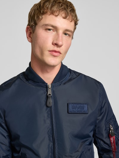 Männermodel trägt dunkelblauen Blouson mit Logo-Anhänger Modell 'MA-1 TT' von Alpha Industries, Label-Patch, Reißverschluss, Nahaufnahme Oberkörper
