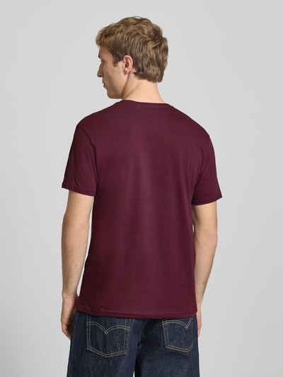 Mężczyznamodel nosi T-Shirt mit Logo und Rundhalsausschnitt von Alpha Industries, bawełna, krój regular fit, bordowy, długość tyłu w rozmiarze M: 68 cm, gładka tekstura, widok całej sylwetki od tyłu