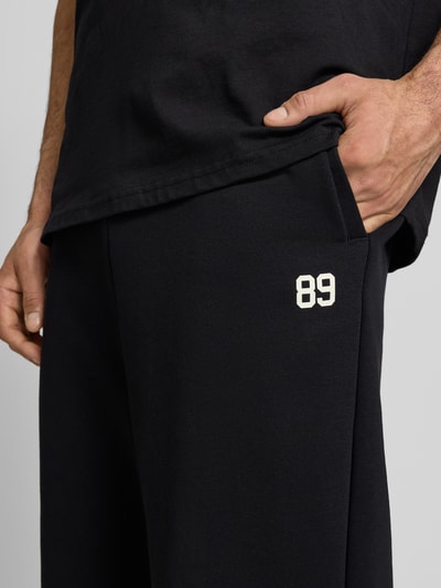 Männermodel trägt Straight Fit Sweatpants mit Gesäßtasche von KARL KANI aus Baumwoll-Mix in Schwarz, Nahaufnahme Oberkörper.