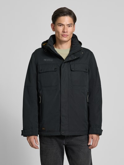 Männermodel trägt zwarte tussenjack met capuchon, statementpatch en rits- plus drukknoopsluiting, Jacke mit Kapuze Modell 'Between Funktion TEXX' van camel active, recht model, vooraanzicht, Nahaufnahme Oberkörper.