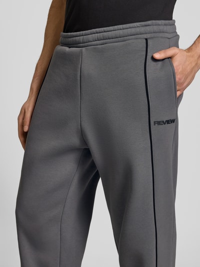 Männermodel trägt Sweatpants mit elastischem Bund und Logo von REVIEW, Reine Baumwolle, Relaxed-Fit, Nahaufnahme Oberschenkel.