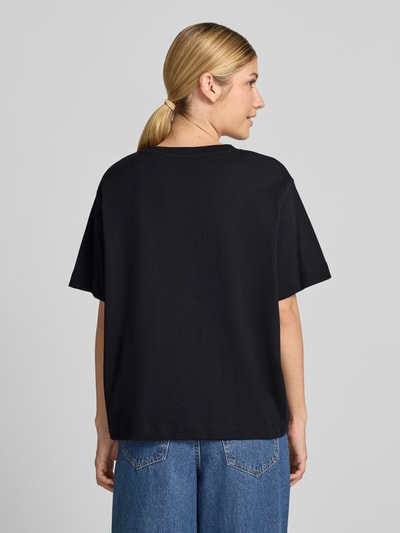 Männermodel trägt czarny damski t-shirt Boxy Fit T-Shirt aus reiner Baumwolle model 'SARA' von VERO MODA, prosta forma, gładka tekstura, Ganzkörperansicht Rückansicht.