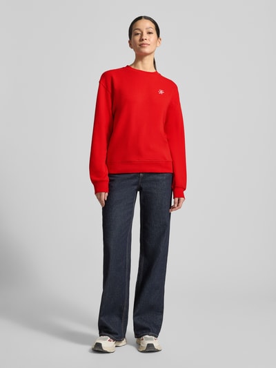 Frauenmodel trägt Regular Fit Sweatshirt aus Baumwoll-Mix von Tommy Hilfiger in Uni-Rot mit Logo-Detail, Rundhals, langarm, Sweatstoff, Ganzkörperansicht von vorne.