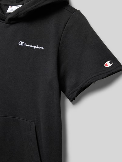 Mädchen trägt Regular Fit T-Shirt mit Kapuze von CHAMPION, schwarzer Baumwoll-Mix, Logo-Stitching, Nahaufnahme Oberkörper